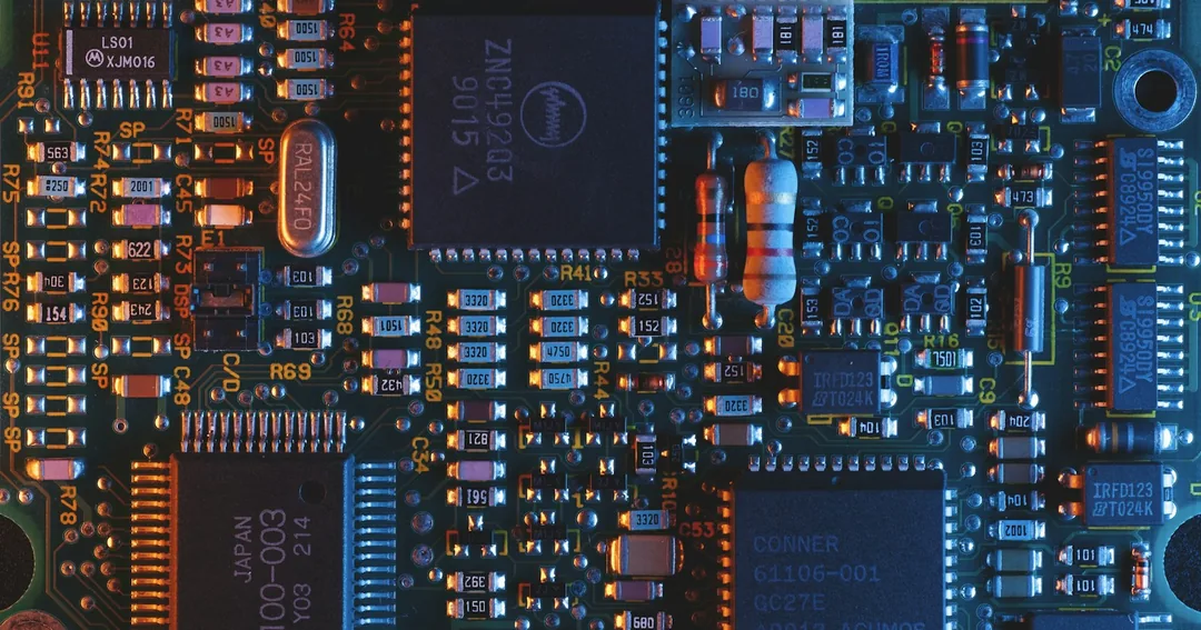 Close-up photograph of a populated circuit board with integrated circuits, resistors and capacitors under blue and orange lighting.